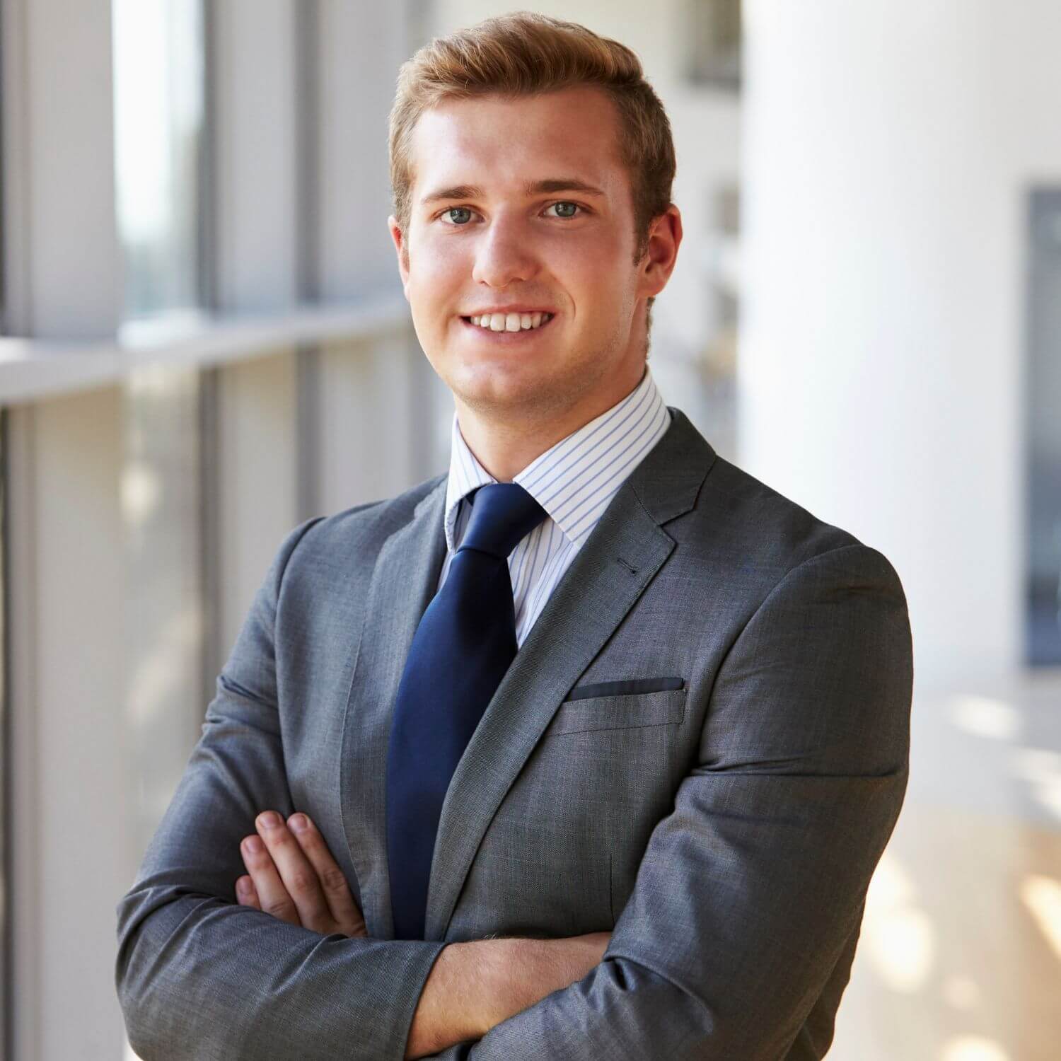 Professionally dressed young man smiling confidently in an office setting.