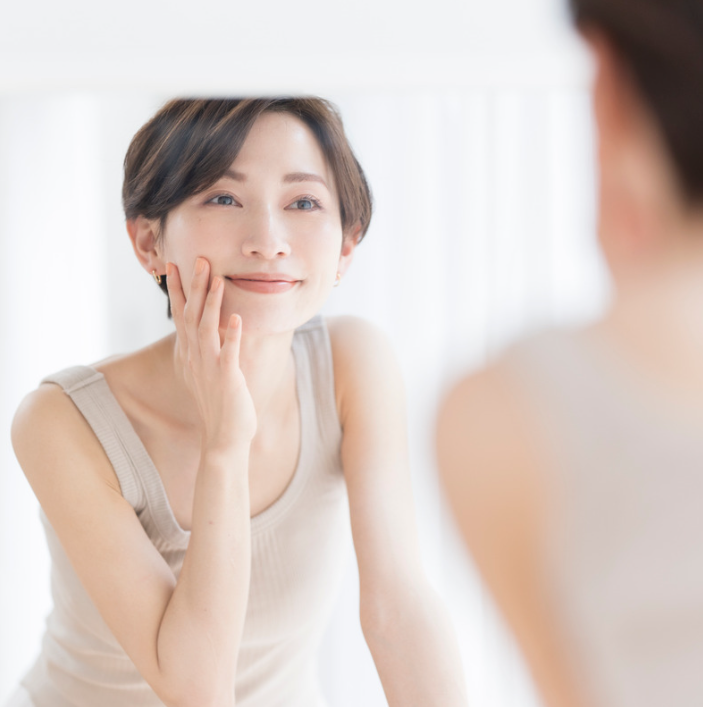 Donna che si guarda allo specchio mentre applica il Liquido Rassodante Portatile sul viso.