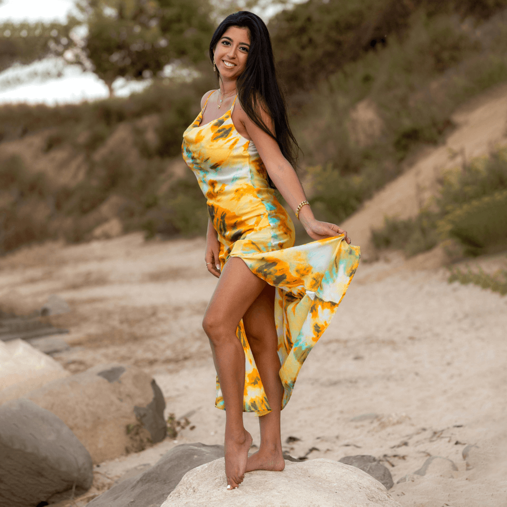 Modella in abito estivo colorato giallo e azzurro posando su una roccia in un ambiente naturale.